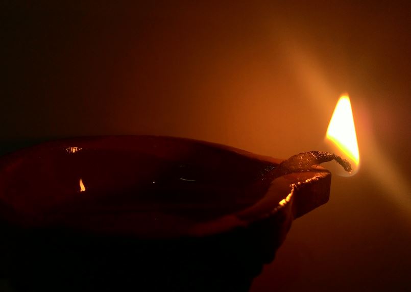 A single lit clay diya (lamp) casting a warm glow in the darkness.